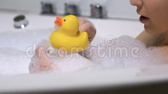 一位性格开朗的年轻女子在泡澡时玩黄色的橡皮鸭放松一下视频的预览图