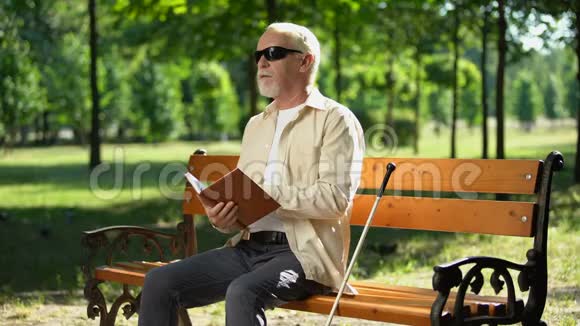 令人沮丧的盲人退休男子无聊的盲文书感到沮丧的独自在公园视频的预览图