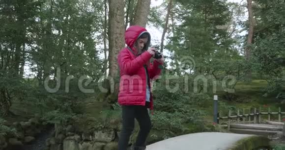 年轻女孩在日本公园的一座混凝土桥上拍摄一条小溪然后走下这座桥视频的预览图