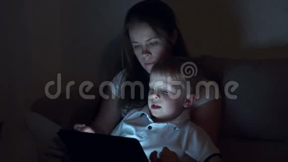 妈妈带着小儿子躺在床上晚上用数码平板电脑读故事视频的预览图