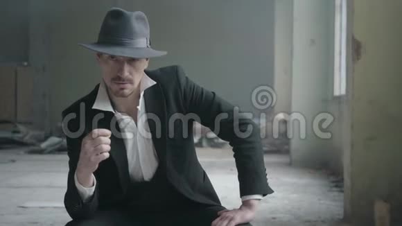 肖像英俊自信的男人戴着帽子把硬币在手指上转动坐在一座废弃的建筑里他的头视频的预览图