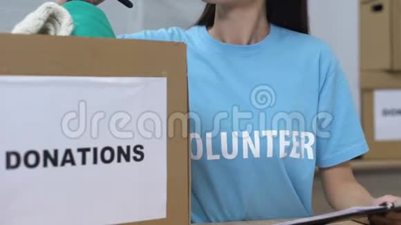 女青年志愿者透过盒子里的捐赠衣物寻找微笑的慈善机构视频的预览图