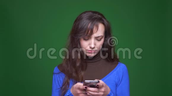 年轻的黑发女学生在绿色背景下专心和认真地使用智能手机视频的预览图