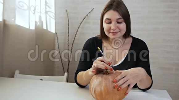 万圣节的概念快乐的女孩坐在一张桌子上用南瓜画眼睛和嘴巴视频的预览图