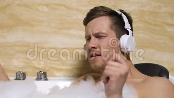 充满欢乐的年轻人在浴缸里躺着耳机听最喜欢的音乐视频的预览图