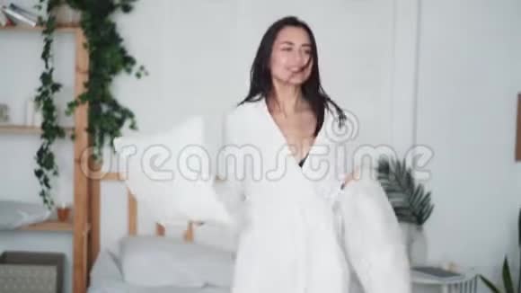 年轻女子在卧室里跳在家里抱着枕头跳舞有趣的视频视频的预览图