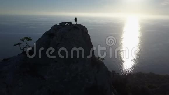 幸福的年轻女子站在高高的山顶上在美丽的夕阳下欣赏美妙的海景女士到达视频的预览图