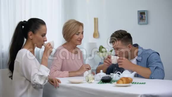 震惊的女人看着婆婆在喝咖啡的时候擦着儿子的嘴视频的预览图