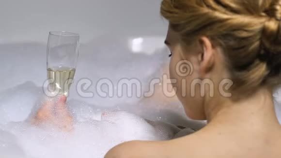 迷人的女人在带泡沫的浴缸里享受香槟享受奢华的放松视频的预览图