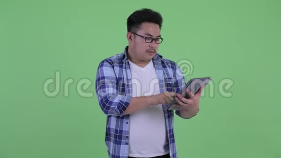 快乐年轻体重超重的亚洲时髦男人使用手机和数码平板电脑视频的预览图
