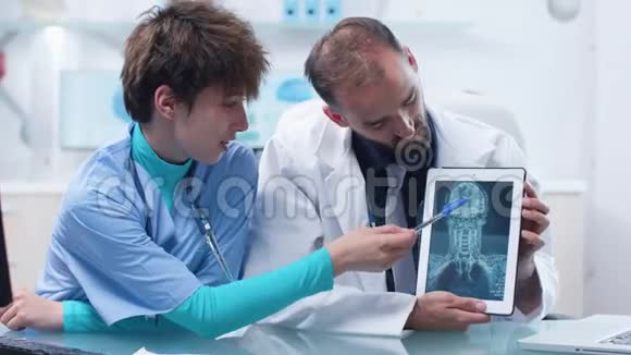 医生和年轻护士在数字平板电脑上看核磁共振CTX线扫描视频的预览图