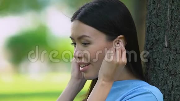漂亮的女人通过无线耳塞听音乐在公园放松视频的预览图
