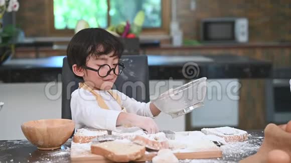 可爱的亚洲小男孩在家里的厨房里用筛子筛面粉准备烘焙面包店和蛋糕泰国k视频的预览图