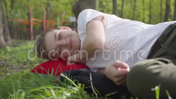 男孩躺在操场附近的草地上在温暖的春日周末放学后心烦意乱或疲倦视频的预览图