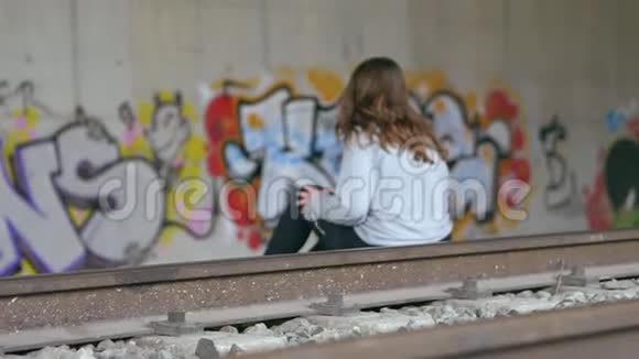 年轻的白人女人棕色头发坐在火车轨道上隧道墙上的涂鸦慢动作视频的预览图