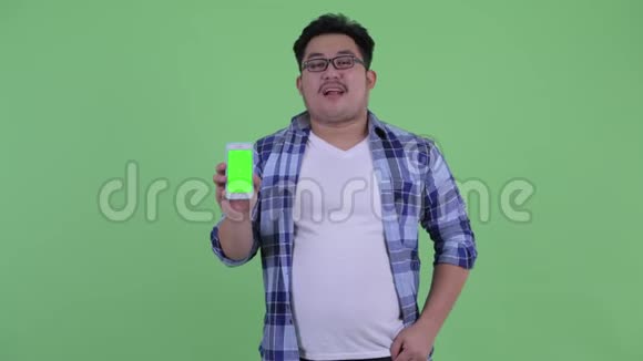 快乐年轻体重超重的亚洲时髦男人带着电话竖起大拇指视频的预览图