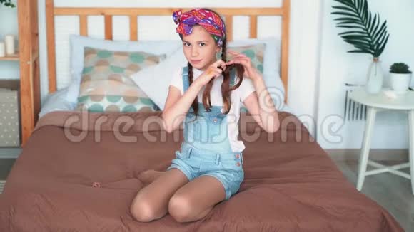 女孩坐在床上梳辫子微笑看镜头慢动作视频的预览图