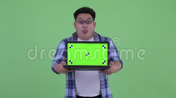 年轻快乐体重超重的亚洲时髦男人带着笔记本电脑看上去很惊讶视频的预览图