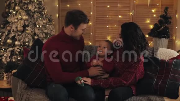 幸福的家庭和小婴儿坐在沙发附近的圣诞树舒适的家庭背景和微笑概念视频的预览图
