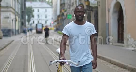 帅气的非裔美国年轻人戴着耳机四处张望一边推着时髦的现代自行车一边走下来视频的预览图
