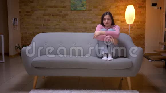 年轻漂亮的棕色白种人女性在一个舒适的沙发上坐着悲伤沮丧和无聊的特写镜头视频的预览图