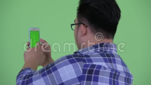 快乐年轻超重的亚洲时髦男人使用电话的后视图视频的预览图