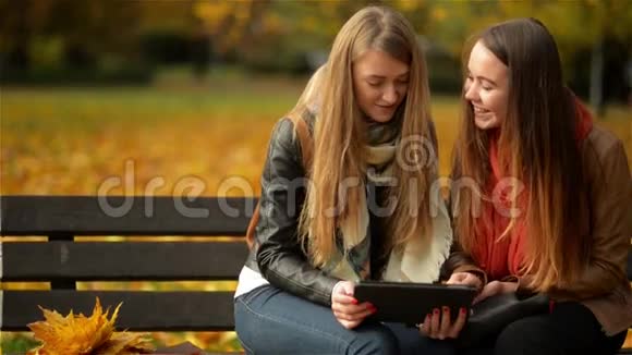 两个有趣的快乐年轻女孩朋友坐在长凳上用平板电脑女人在Pad电脑上嬉笑打闹视频的预览图