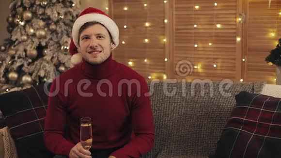 戴着圣诞帽的白人笑容可掬的肖像和拿着一杯香槟坐在上面的冬季毛衣视频的预览图