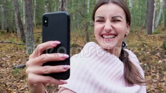 一位快乐的年轻女子在春天的森林里愉快地打电话自拍并微笑着慢镜头特写视频的预览图