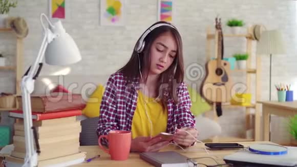 积极美丽的亚洲女孩留着长发在现代家庭的客厅里带着耳机听音乐和音乐视频的预览图