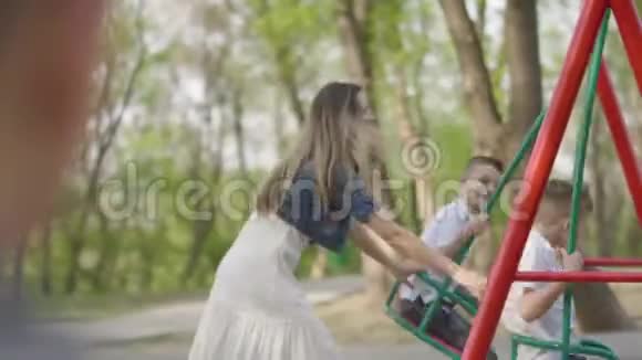 快乐的母亲推着笑两个儿子在公园里荡秋千户外娱乐活动视频的预览图