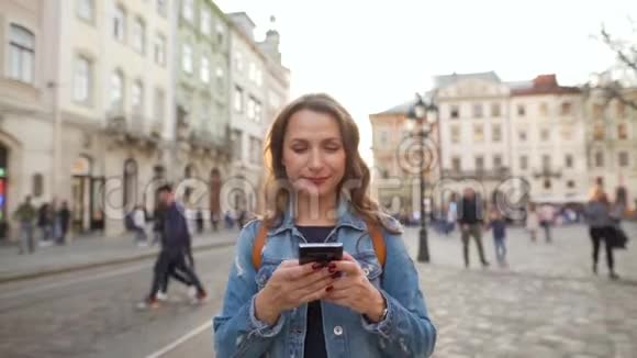 日落时分女人用智能手机走在老街上黄色有轨电车在后台交流社会视频的预览图