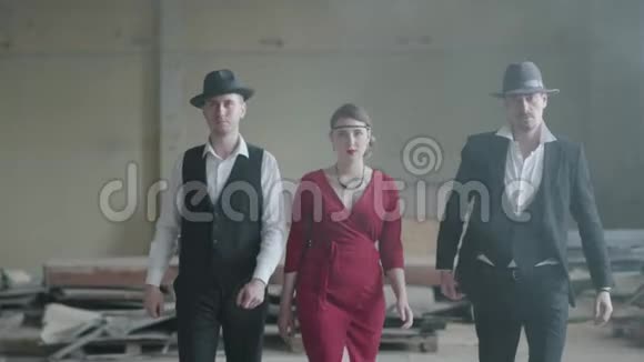 两个自信的男人戴着帽子穿着西装女人穿着红色的衣服在一座废弃的建筑里朝镜头走去黑手党视频的预览图