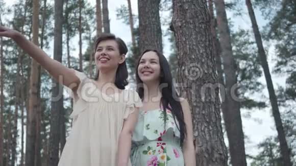 两位可爱的年轻女子站在松林的背景下穿着礼服看着令人惊叹的景色视频的预览图