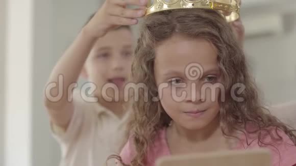 可爱的男孩把皇冠放在可爱的卷发女孩的头上看着镜子勇敢的男孩关心一个美丽的视频的预览图
