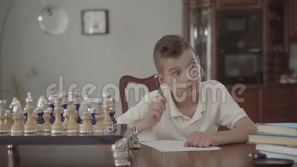 一张可爱体贴的家伙坐在家里的桌子上的肖像男孩恍然大悟在一片土地上写了些东西视频的预览图