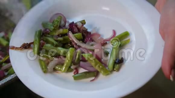 女人的手把炒好的青豆和洋葱放在白色的盘子里视频的预览图