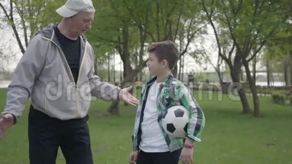 那个穿着格子衬衫的小男孩和积极的老人在公园里踢足球孙子和视频的预览图