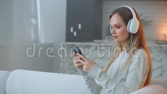 小女孩听着耳机里的音乐看着智能手机的屏幕在家放松视频的预览图