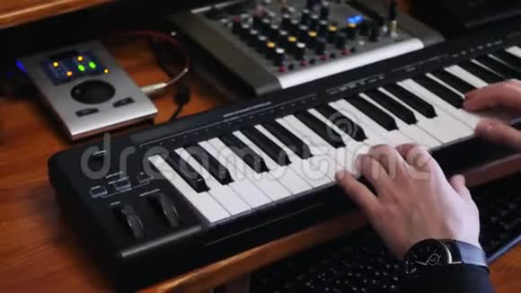 双手演奏MIDI电子琴同时在家庭录音室用混音板和音波创作流行摇滚歌曲视频的预览图