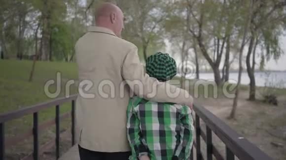 在公园的桥上祖父和孙子背对着镜头走着那个男人拥抱视频的预览图