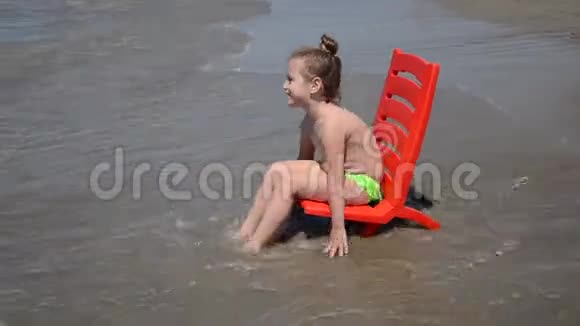 在沙滩上坐在海边的椅子上和海浪玩耍的小女孩视频的预览图