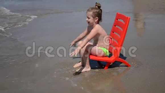在沙滩上坐在海边的椅子上和海浪玩耍的小女孩视频的预览图