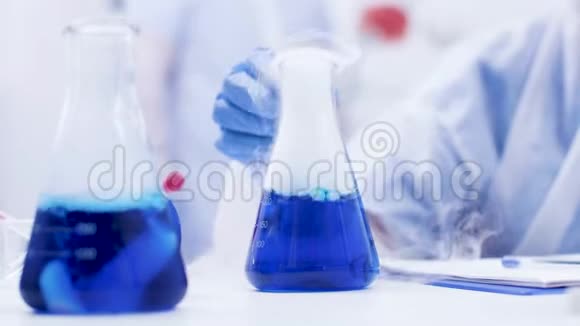 一个实验室里的女科学家在瓶子里捡起并拿着一种冒烟的蓝色液体视频的预览图
