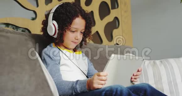 带耳机的非裔美国男孩在医院大堂玩数字平板电脑游戏的正面景色视频的预览图