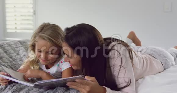 母亲和女儿在舒适的家里卧室里看故事书视频的预览图