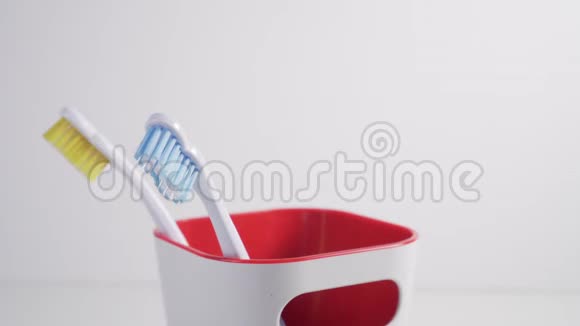 一个年轻人把一把红色刚毛的牙刷放进浴室的塑料杯里视频的预览图