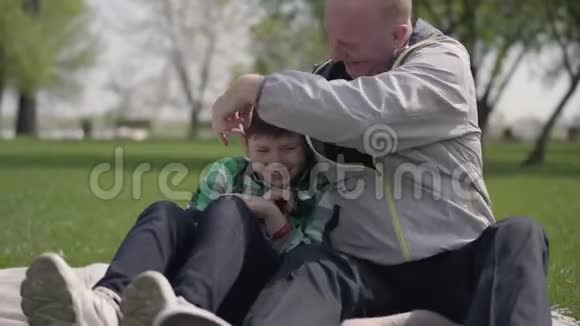 肖像可爱的老人和孙子坐在公园的毯子上挠着小男孩孩子是视频的预览图