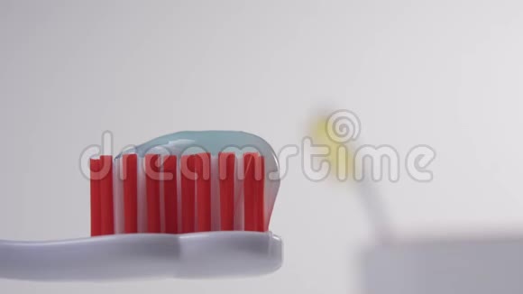 白色牙刷上面有红色刚毛和蓝色牙膏在背景中一只手把一把蓝色牙刷放进玻璃杯里视频的预览图