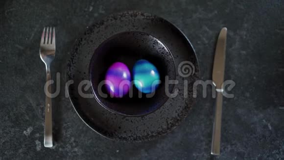 两个彩色复活节彩蛋在一个黑色盘子在黑暗的背景上的俯视图视频的预览图